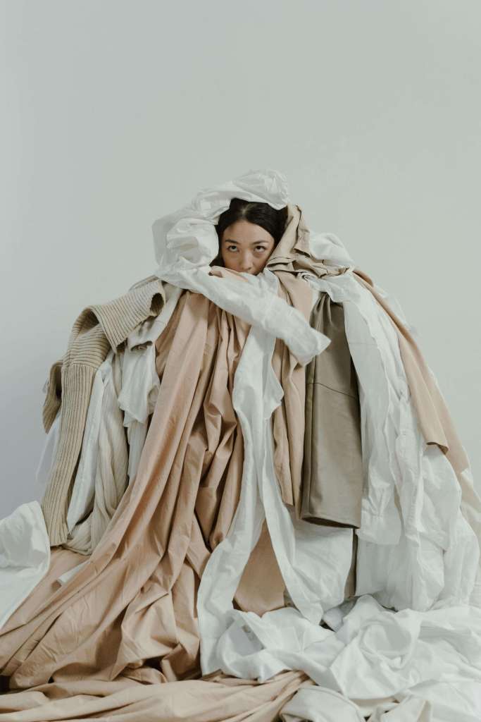 woman covered in pile of clothes feels like she has nothing to wear